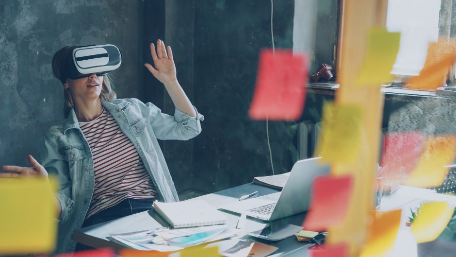 Žena s VR headsetom razmišlja uz laptop i bilješke